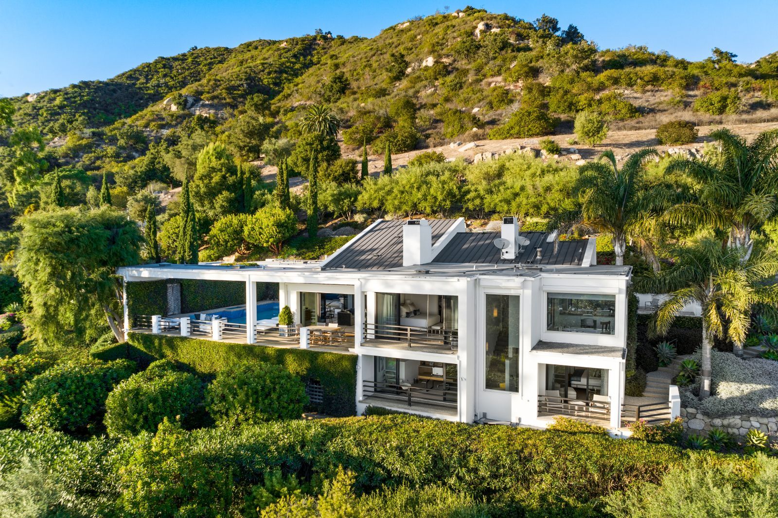 A 2-story modernist home resting on a hillside of lush grass and trees.